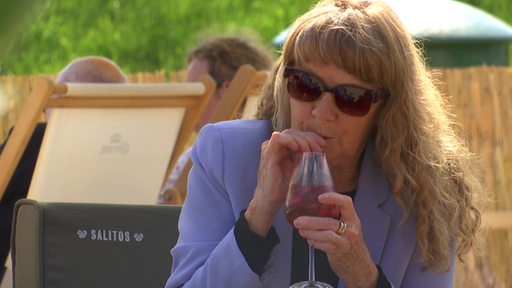 Eine Frau mit Sonnenbrille trinkt ein Getränk in einer Aussengastro.