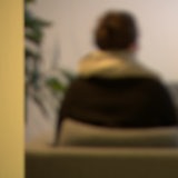 Eine unkenntlich gemachte Frau sitzt in einem Sessel für ein Interview mit dem Rücken zur Kamera.
