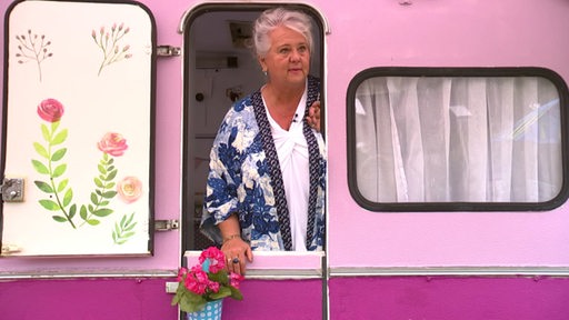 Eine Frau steht in der Tür eines pinken Wohnwagens.