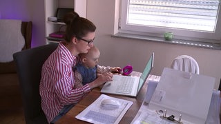 Eine Mutter arbeitet von Zuhause an ihrem Laptop und ihr Baby sitzt auf ihren Schoss. 