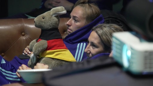 Zwei Mädels schauen gespannt das Fußballspiel der Frauen WM mit einem Känguru in Deutschlandflagge. 