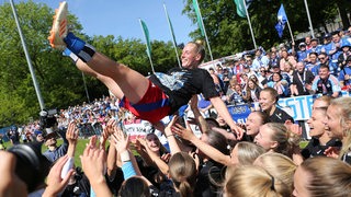 Fußball-Spielerinnen des HSV werfen eine Mitspielerin in die Luft beim Jubel über ihren Aufstieg in die Bundesliga.
