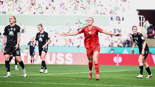 Werders Fußballerinnen stehen enttäuscht auf dem Rasen beim Pokal-Finale, als Bayern-Spielerin Lea Schüller mit ausgebreiteten Armen ihr Tor feiert.