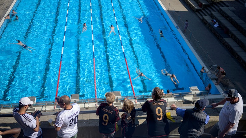 Menschen mit Fußball-Trikots mit der Aufschrift "Füllkrug" schauen auf einm Schwimmbecken, in dem Menschen schwimmen.
