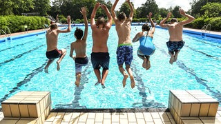 Schüler springen gemeinsam ins Schwimmbecken. (Symbolbild)