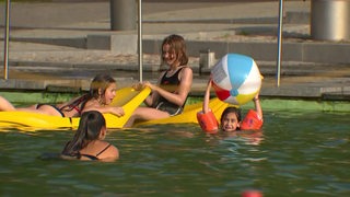 Mehrere Kinder baden in einem Freibad mit Bällen und Wassermatratzen. 