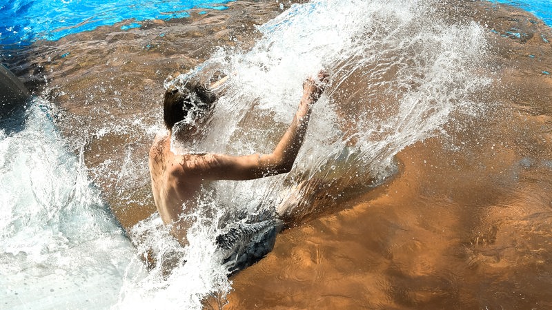 Ein Junge rutscht in ein Schwimmbecken. Wasser spritzt herum.