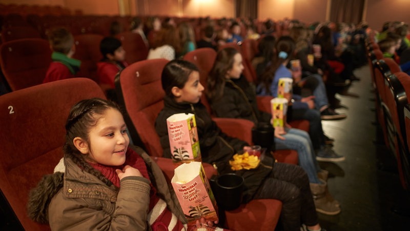 Kinder sitzen mit Popcorn-Tüten im Kino (Symbolbild)