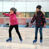 Zwei Mädchen fahren mit Schlittschuhen auf einer Eisbahn 