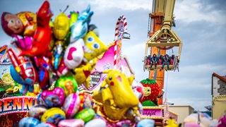 Bunte Luftballontiere sind unscharf im Vordergrund zu sehen. Im Hintergrund ist ein Karussell zu sehen, in dem Menschen sitzen.