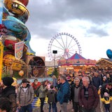 Das Riesenrad ist im Hintergrund zu sehen. Im Vordergrund laufen Besucher über den Freimarkt.