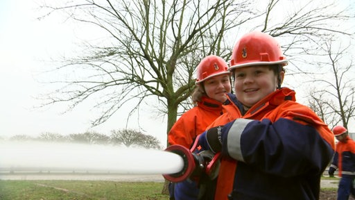 Zwei Kinder in Feuerwehrkleidung beim Löschen.