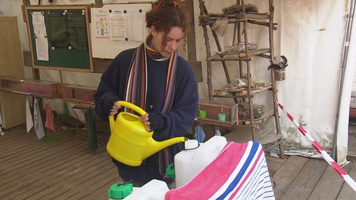 Eine Person gißt mit einer Gießkanne Wasser in einen Kanister.