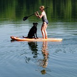 Eine Frau beim Stand-Up-Paddling mit Hund auf einem See.