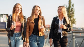 Drei Frauen unterhalten sich lächelnd und spazieren in der Sonne