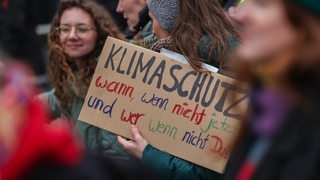 Junge Menschen, eine junge Frau hält ein Schild in den Händen mit der Aufschrift: Klimaschutz, wann, wenn nicht jetzt und wer, wenn nicht Du?