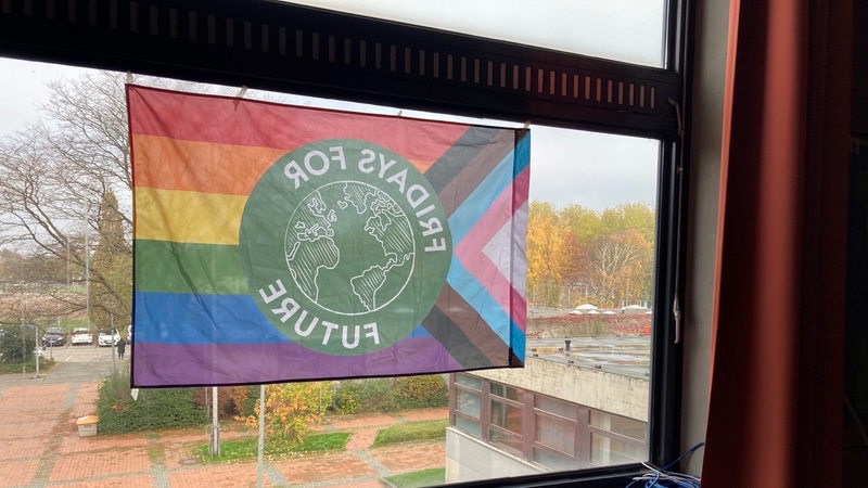 An einem Fenster hängt eine Regenbogenfahne mit Fridays for Future Logo.