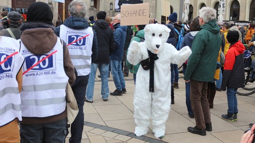Eine Person im Eisbären-Kostüm steht zwischen Demonstranten und hält ein Schild.