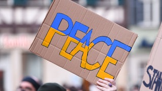 ine Demonstrantin zeigt ein Schild mit der Aufachrift, Peace! 