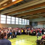 Zahlreiche Kinder und Jugendliche stehen vor einer Band in einer Sporthalle.