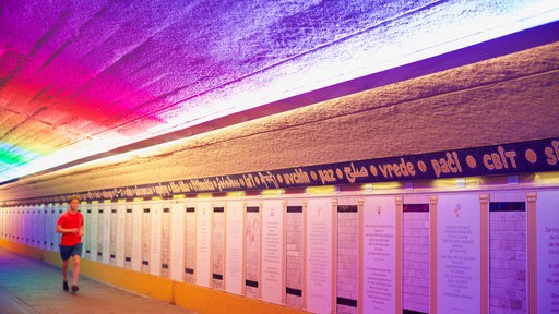 Jogger vor bunt ausgeleuchteten Texttafeln in einem Tunnel