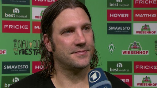 Werders Ex-Kapitän Torsten Frings steht vor einer Werbetafel beim Interview.