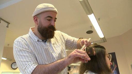 Der Friseurmeister Abdulrhman Cakar schneidet seiner Kundin die Haare. 