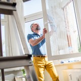 Ein Mann putzt in seiner Wohnung die Fenster.