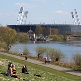 Menschen geniessen die Sonne am Osterdeich an der Weser, hinten das Weserstadion vom SV Werder Bremen.