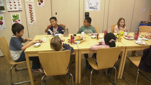 Mehrere Kinder sitzen an einem langen Tisch und frühstücken zusammen.