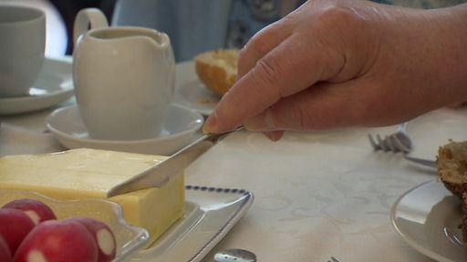 Auf einem gedeckten Frühstückstisch wird ein Stück Butter abgeschnitten.