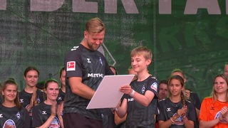 Zu sehen ist Niklas Füllkrug mit einem Kind auf einer Bühne beim Tag der Fans. 
