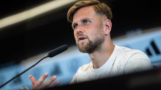 Niclas Füllkrug sitzt bei einer Pressekonferenz auf dem Podium vor einem Mikro.