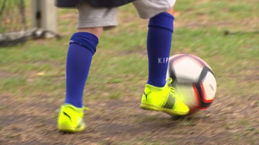 Ein Junge spielt Fussball. Er trägt gelbe Schuhe und blaue Stutzen.