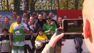 Fußballer Ailton posiert mit Daumen hoch gemeinsam mit Fans für ein Foto bei seinem Comeback beim TSV Bassum.