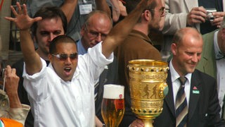 Werder-Stürmer Ailton jubelt mit ausgebreiteten Armen auf dem Bremer Rathaus-Balkon, neben ihm Trainer Thomas Schaaf und der goldene Pokal.