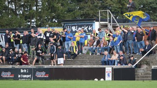 Mehrere Fans von Atlas Delmenhorst feuern ihre Mannschaft während eines Spiels an.