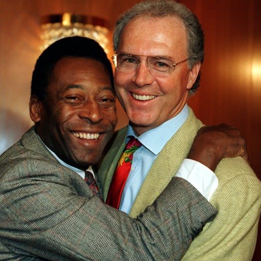 Die Fußball-Legenden Franz Beckenbauer und Pelé umarmen sich 1996 bei einer Begegnung strahlend.