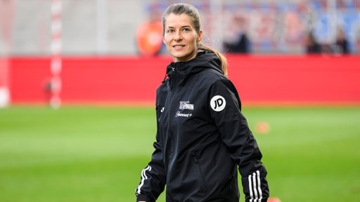 Fußball-Trainerin Marie-Louise Eta von Union Berlin geht lächelnd an der Seitenlinie entlang.