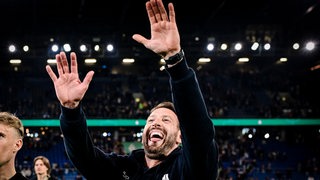 Der Fußball-Trainer von Arminia Bielefeld, Mitch Kniat, reißt nach dem Einzug ins Finale des DFB-Pokals lachend die Arme hoch und streckt leicht die Zunge heraus.