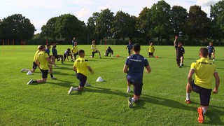 Die Mannschaft des Bremer SV kniet in einem Kreis auf dem Fußballfeld und macht Dehnübungen.