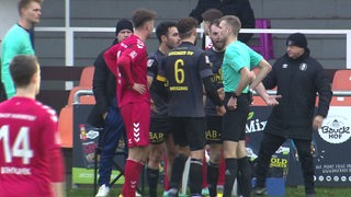 Fußballer des Bremer SV und der Eintracht Norderstedt stehen um den Schiedsrichter herum und beschweren sich über die Rote Karte.