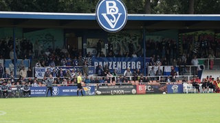 Malte Seemann steht im Tor, die Fans verfolgen das Spiel von der Tribüne.