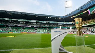 Der DFB-Pokal steht im Weser-Stadion auf einem Podest. Im Hintergrund ist ein Flutlichtmast des Stadions zu sehen.