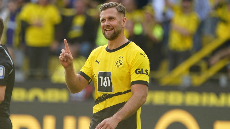 Dortmunds Stürmer Niclas Füllkrug hebt grinsend auf dem Spielfeld den Zeigefinger.
