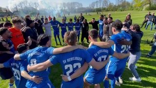 Fußball-Spieler und Trainer der SV Hemelingen stehen Arm in Arm im Kreis und hüpfen vor Freude über die Meisterschaft.