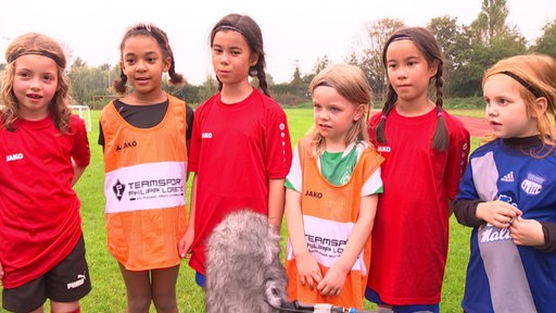 Sechs Bremer Mädchen im Alter zwischen fünf und acht Jahren erzählen auf dem Fußballplatz einem TV-Team von ihrer Mädchen-Fußballgruppe.