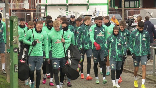 Die Spieler von Werder Bremen laufen in ihren Trikots die Straße entlang.