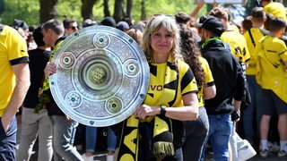 Ein weiblicher Dortmund-Fan hält eine Meisterschale aus Plastik in die Kamera.