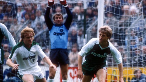 Die Fußball-Profis Winfried Schäfer von Gladbach und Klaus Fichtel von Werder Bremen sind im Pokal-Halbfinale 1984 im Zweikampf, hinter ihnen reckt sich Werder-Torwart Dieter Burdenski.